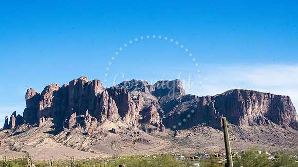Panoramic view of the Superstition Mountains in Arizona under a bright blue sky with desert foreground and saguaros